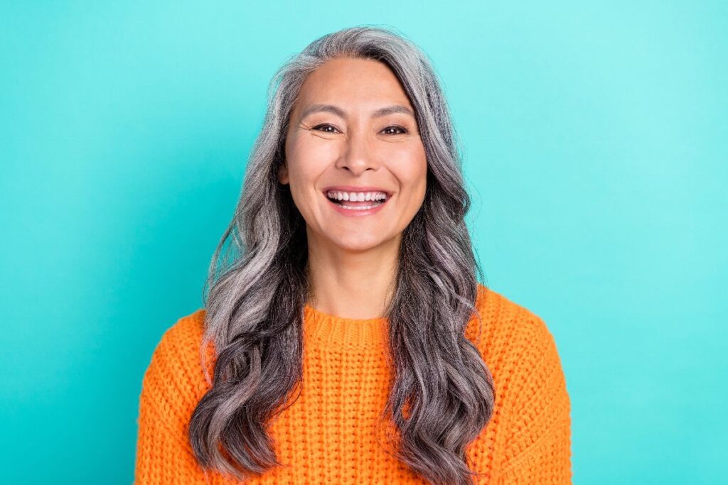 Donna sorridente in posa su sfondo azzurro, con maglioncino arancione.