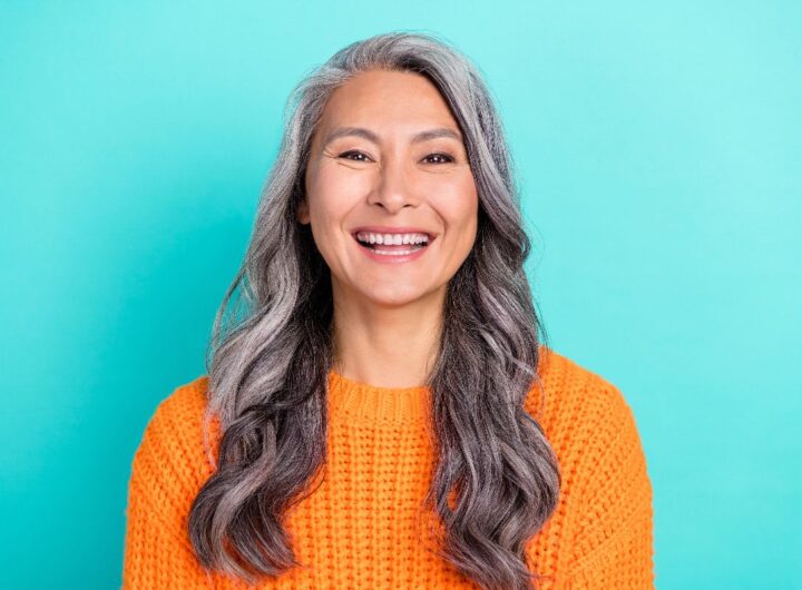Donna sorridente in posa su sfondo azzurro, con maglioncino arancione.