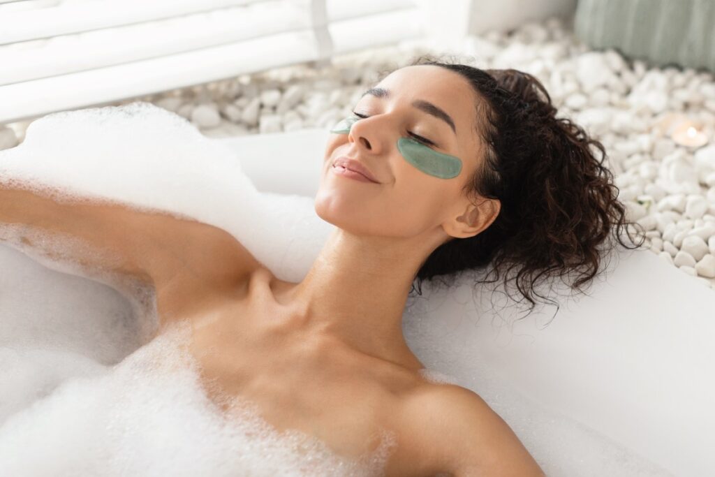 Ragazza si rilassa nella vasca da bagno mentre applica una maschera per le occhiaie.