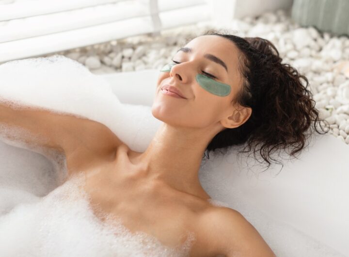 Ragazza si rilassa nella vasca da bagno mentre applica una maschera per le occhiaie.