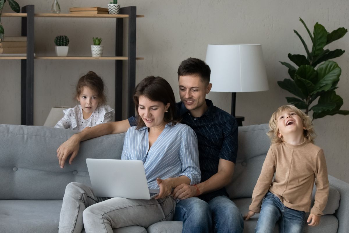Famiglia felice guarda il computer comodamente seduta sul divano di casa.