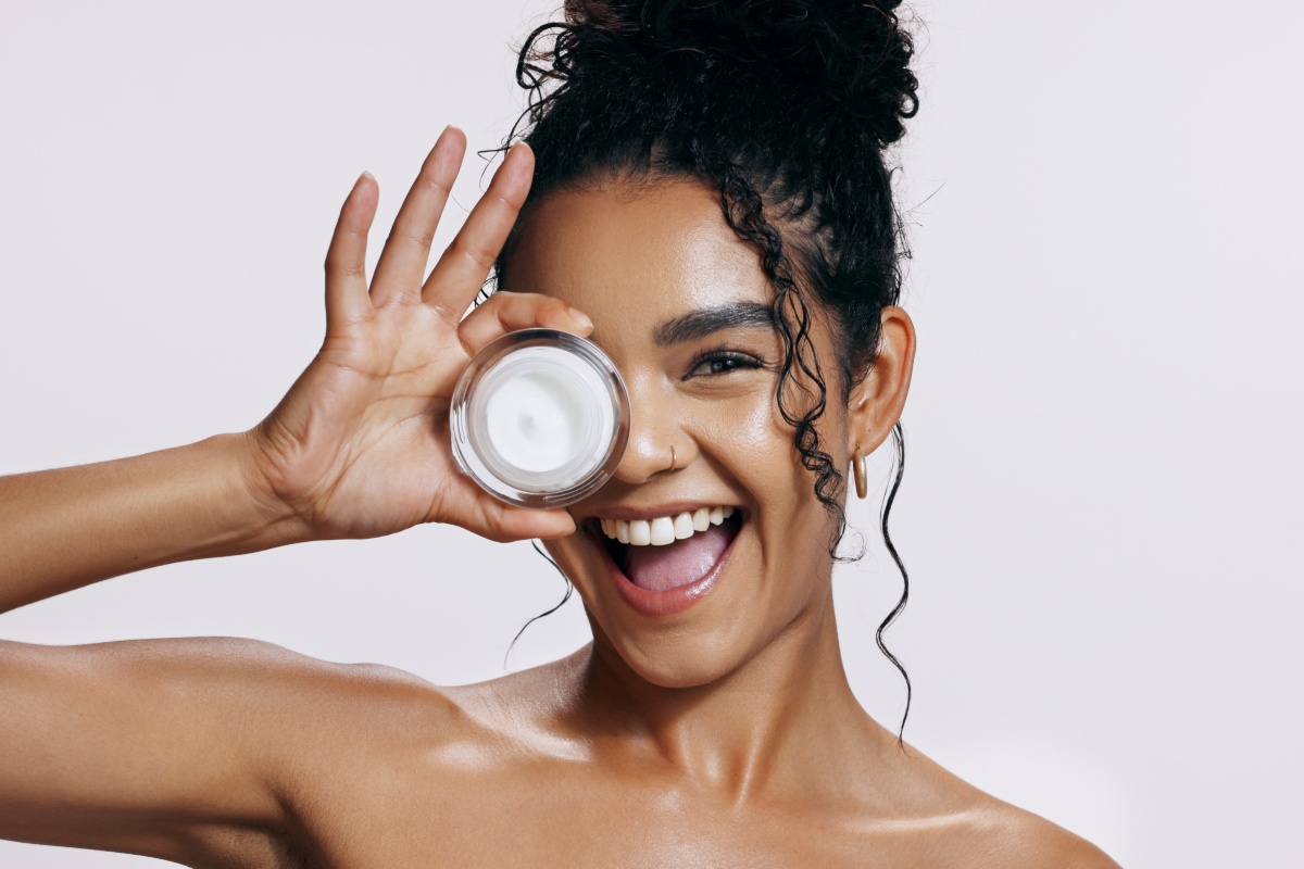 Skincare e sorriso: ragazza sorridente mostra una crema viso.