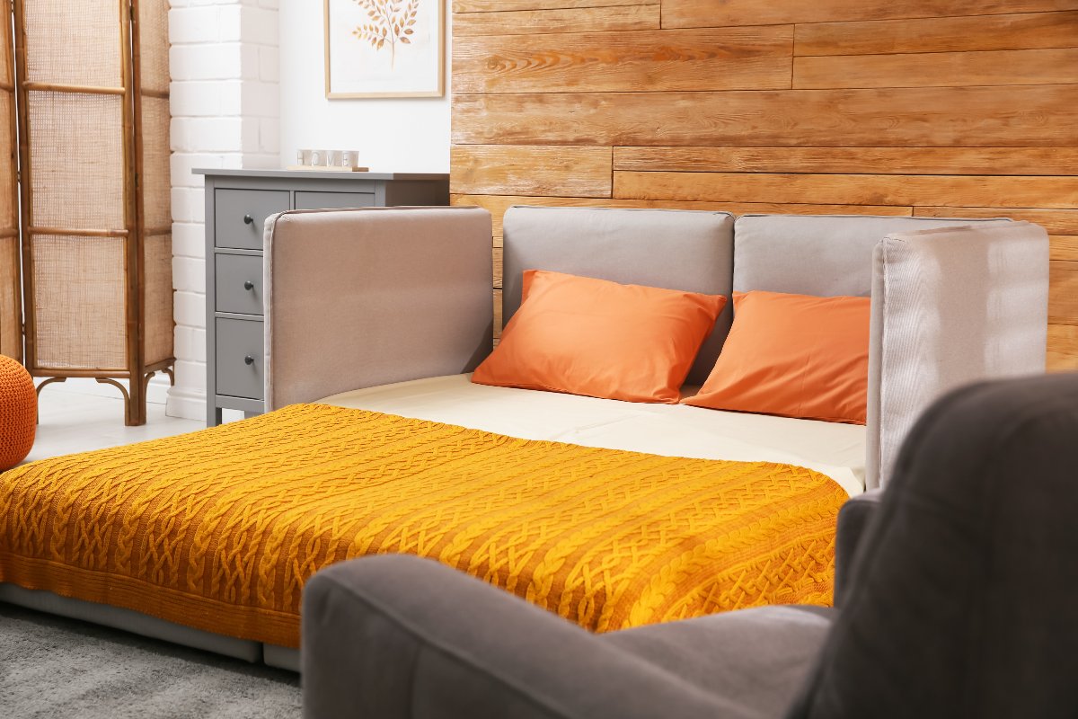 Divano letto accessoriato con una coperta e morbidi cuscini arancioni.
